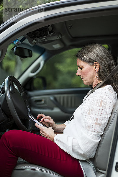 Frau sitzt in ihrem Auto und benutzt ihr Smartphone; Bothell  Washington  Vereinigte Staaten von Amerika