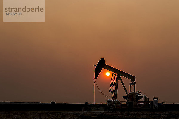 Silhouette eines Pumpjacks mit einem glühend warmen Sonnenball im Hintergrund  westlich von Airdrie; Alberta  Kanada