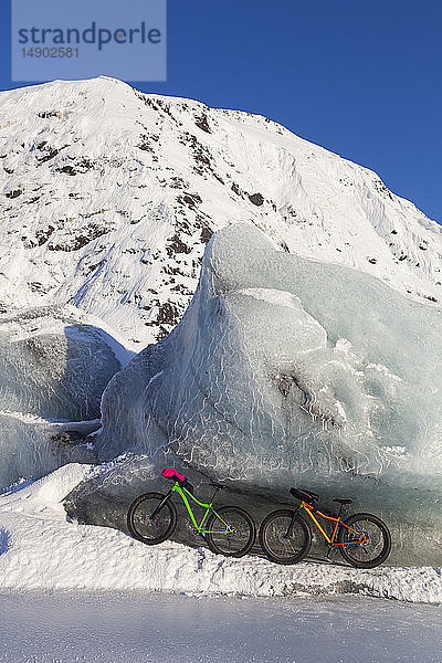 Fatbikes  907 fat tire bike und Fatback fat tire bike  ruhen gegen einen riesigen Eisberg im Winter auf dem Portage Lake  Chugach National Forest; Portage  Alaska  Vereinigte Staaten von Amerika