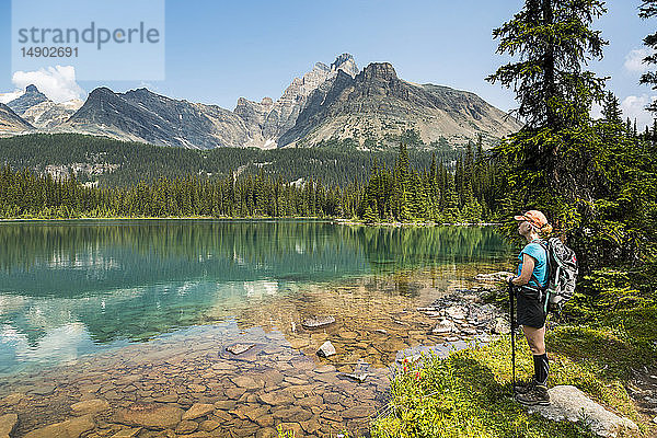 Wanderin am Ufer eines Bergsees  in dem sich eine Bergkette mit blauem Himmel spiegelt; British Columbia  Kanada