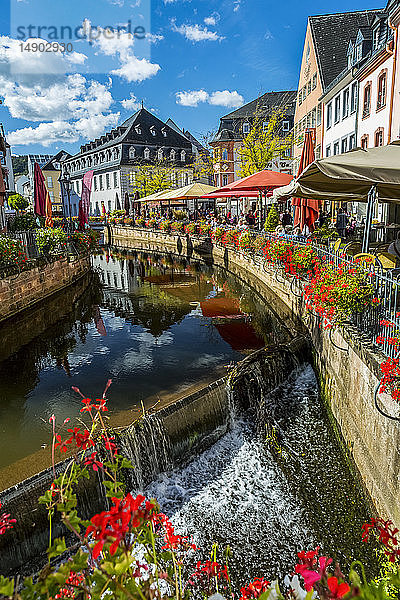 Kanal mit Wasserfällen in einem bunten Dorf mit Blumenkästen entlang des Geländers und blauem Himmel mit Wolken; Saarburg  Deutschland