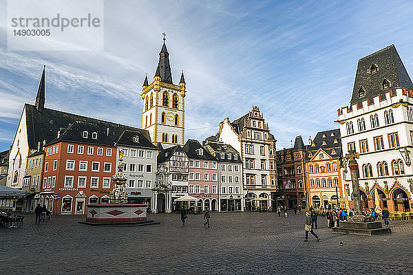 Spaziergänger auf dem mittelalterlichen Marktplatz in einem Dorf mit dekorativem Brunnen  bunten Gebäuden und einem großen Uhrenturm mit blauem Himmel und Wolken; Trier  Deutschland