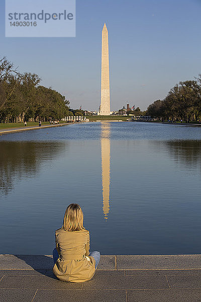 Tourist sitzt am Rande des spiegelnden Beckens mit Blick auf das Washington Monument  aufgenommen vom Lincoln Monument; Washington D.C.  Vereinigte Staaten von Amerika