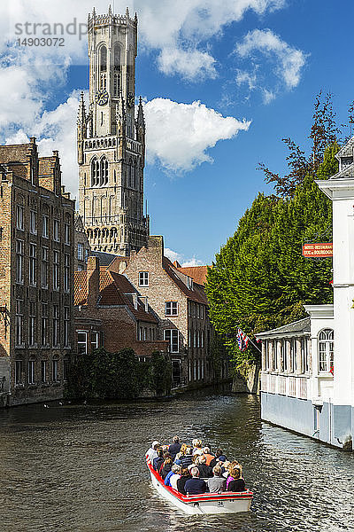 Kleines Ausflugsboot mit Menschen in einer Gracht mit großem gotischen Kirchturm im Hintergrund; Brügge  Belgien