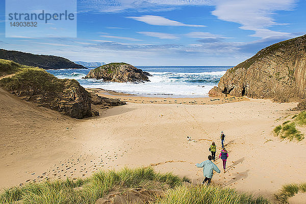 Eine Familie läuft mit ihrem Hund über den Sand und genießt den Strand an der irischen Küste; Irland