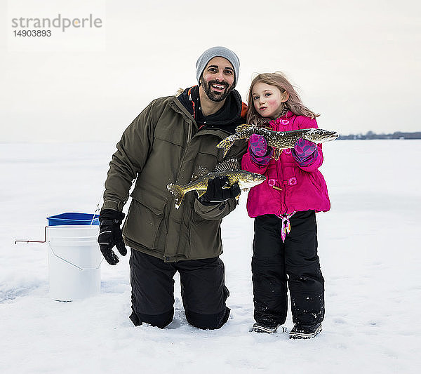 Vater und junge Tochter zeigen ihren Fang  bevor sie ihn beim Eisfischen am Lake Wabamun freilassen; Wabamun  Alberta  Kanada