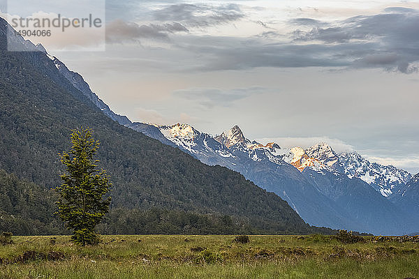 Bewölkter Sonnenuntergang über verschneiten Bergen im Eglinton Valley; Südinsel  Neuseeland