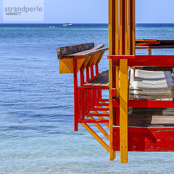 Bunt bemalter Steg mit Liegestühlen und dem Karibischen Meer mit einem Boot in der Ferne; Roatan  Bay Islands Department  Honduras