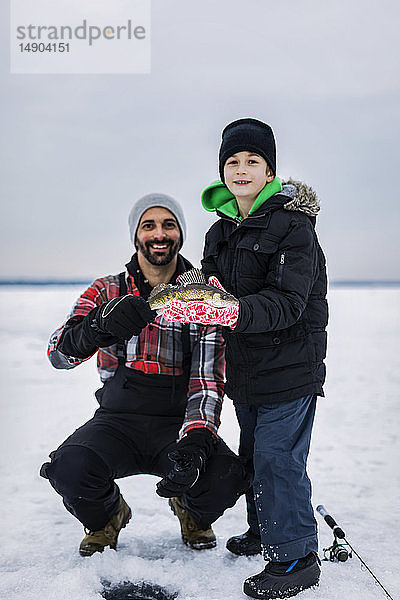 Vater und kleiner Sohn zeigen ihren Fang eines Zander  bevor sie ihn beim Eisfischen im Wabamun-See freilassen; Wabamun  Alberta  Kanada