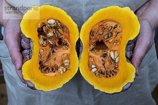 Nahaufnahme einer Person  die einen Kürbis mit halbiertem orangefarbenem Fleisch hält.