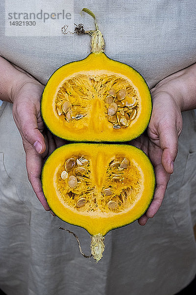 Nahaufnahme einer Person  die einen Kürbis mit halbiertem orangefarbenem Fleisch hält.