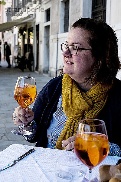 Frau sitzt an einem Tisch im Freien und hält ein Glas Aperol Spritz