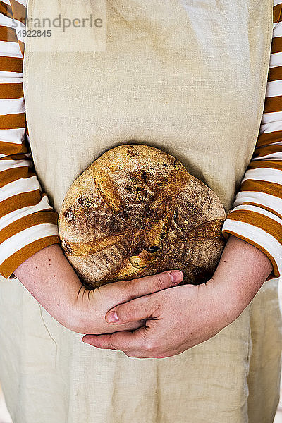 Nahaufnahme einer Person  die einen frisch gebackenen runden Laib Brot in der Hand hält.