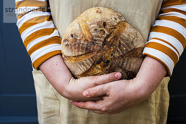 Nahaufnahme einer Person  die einen frisch gebackenen runden Laib Brot in der Hand hält.