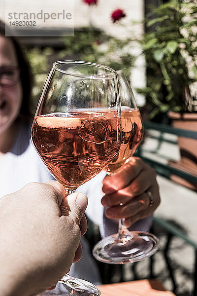 Frau und eine weitere Person sitzen an einem Tisch und stoßen mit Weingläsern von Aperol Spritz an.