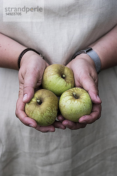 Nahaufnahme einer Person  die drei grüne Äpfel hält.