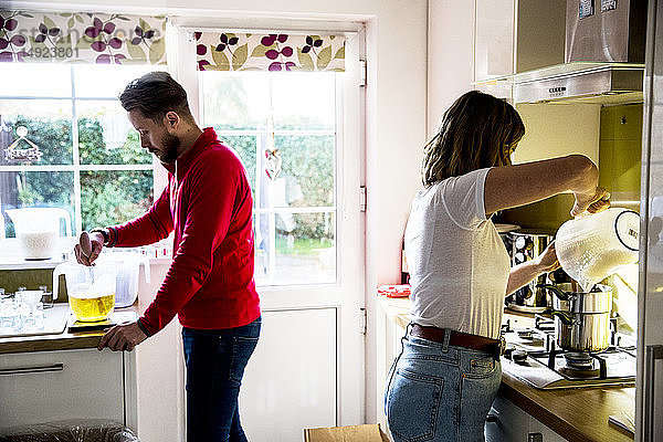 Mann und Frau stehen in einer häuslichen Küche und machen Glaskerzen.
