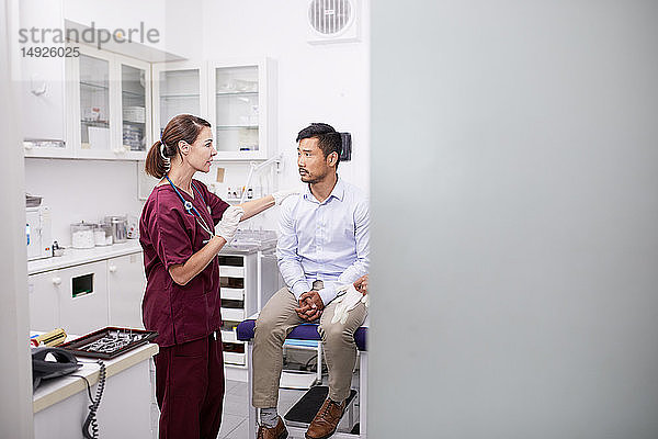 Ärztin im Gespräch mit einem männlichen Patienten im Untersuchungsraum einer Klinik