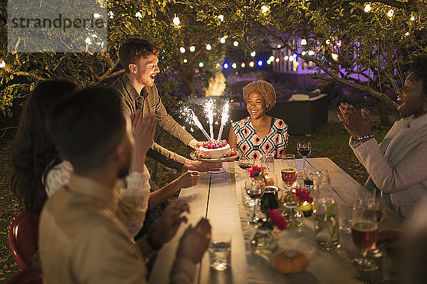Glückliche Freunde feiern Geburtstag mit Wunderkerze Kuchen im Garten Partei Tabelle