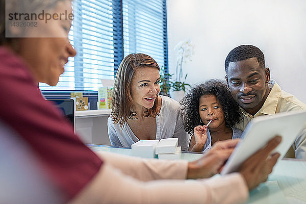 Arzt mit digitalem Tablet im Gespräch mit der Familie in der Arztpraxis