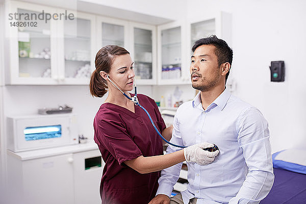 Eine Krankenschwester benutzt ein Stethoskop bei einem männlichen Patienten im Untersuchungsraum einer Klinik