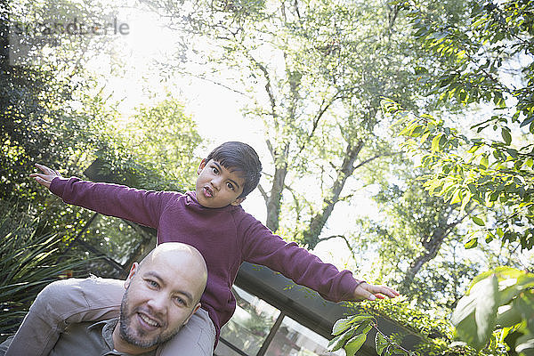 Porträt verspielter Vater  der seinen Sohn im Hinterhof auf den Schultern trägt