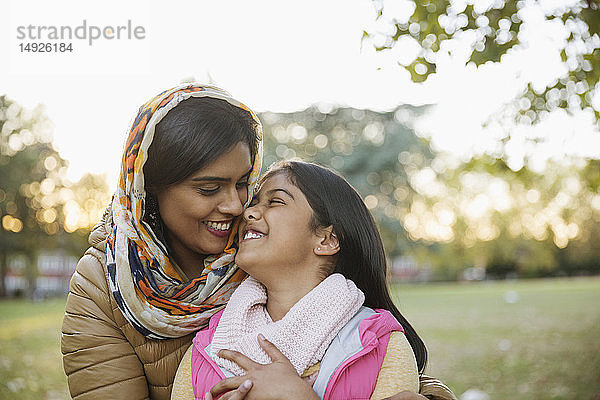 Liebevolle  glückliche muslimische Mutter im Hidschab  die ihre Tochter im Herbstpark umarmt