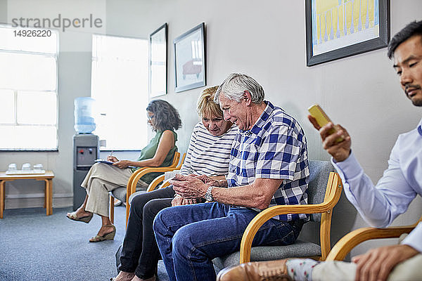 Ein älteres Ehepaar benutzt ein Smartphone im Wartezimmer einer Klinik