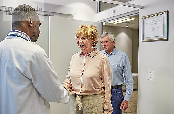 Arzt begrüßt älteres Ehepaar in der Arztpraxis