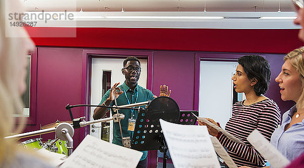 Männlicher Dirigent leitet Frauen beim Singen im Aufnahmestudio