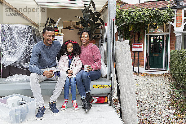 Porträt einer glücklichen Familie beim Teetrinken auf der Ladefläche eines Umzugswagens vor dem neuen Haus