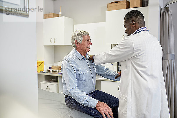 Männlicher Arzt  der einen älteren Patienten im Untersuchungsraum einer Klinik untersucht