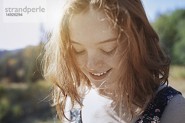 Lächelnde junge Frau mit Sommersprossen blickt nach unten