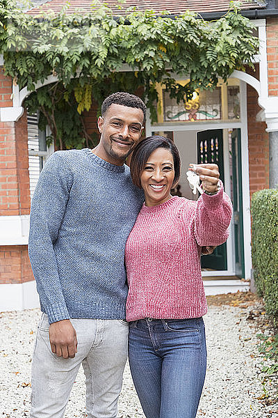 Porträt eines glücklichen Paares mit Hausschlüsseln vor einem neuen Haus