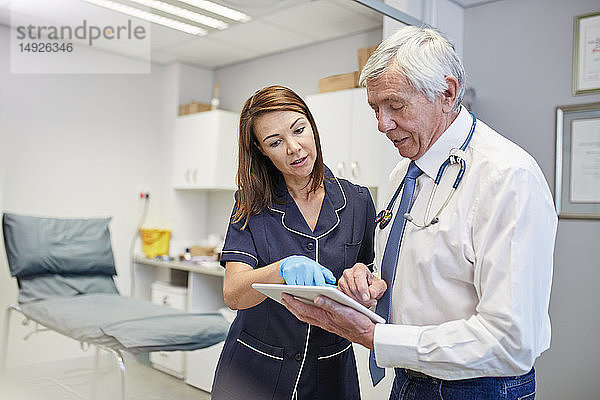 Arzt und Krankenschwester mit digitalem Tablet im Gespräch im Untersuchungsraum einer Klinik