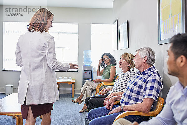 Ärztin im Gespräch mit wartenden Patienten im Wartezimmer einer Klinik