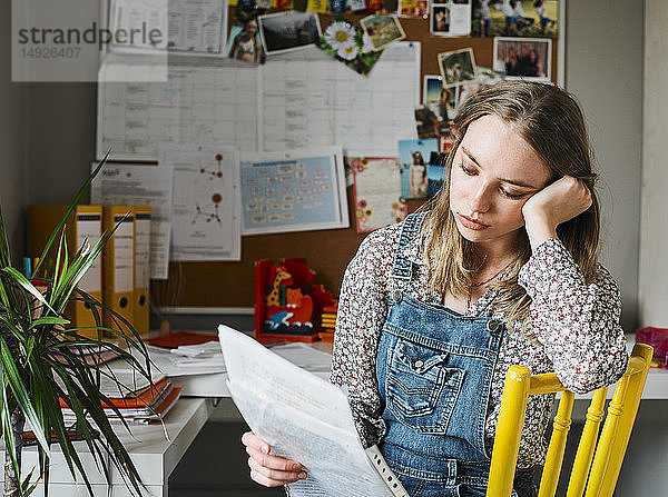 Konzentrierte junge Frau arbeitet im Büro zu Hause und liest Papierkram