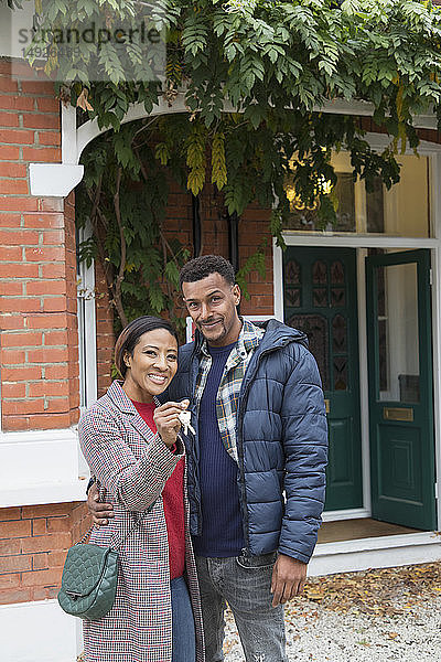 Porträt selbstbewusstes Paar mit Hausschlüssel vor neuem Haus