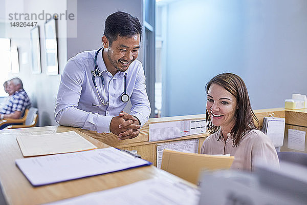 Ein lächelnder Arzt und eine Arzthelferin besprechen die Krankenakte in einer Klinik