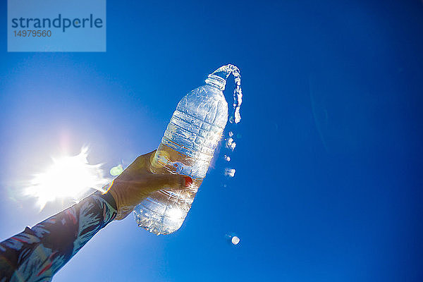 Frau hält Wasserflasche gegen die Sonne