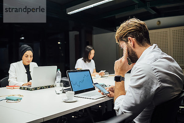 Geschäftsfrau betrachtet Laptop und Smartphones am Konferenztisch