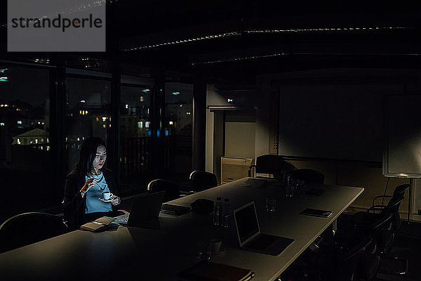 Junge Geschäftsfrau  die nachts im Büro sitzt und auf ihren Laptop schaut