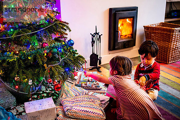 Mädchen und männliches Kleinkind spielen am Wohnzimmer-Weihnachtsbaum