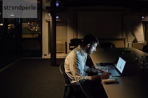 Mittlerer erwachsener Geschäftsmann  der nachts im Büro sitzt und auf seinen Laptop schaut