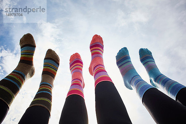 Drei junge Frauen in gestreiften Socken mit gegen den sonnenbeschienenen Himmel erhobenen Beinen  Schrägansicht der Beine