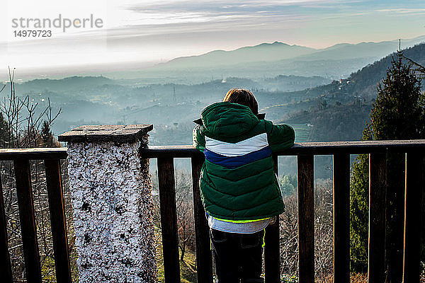 Junge blickt vom Balkon auf die Landschaft des Bergtals  Rückansicht  Piani Resinelli  Lombardei  Italien