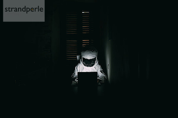 Astronaut mit Laptop in dunklem Raum