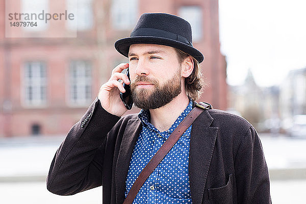 Mann in Trilby macht Smartphone-Anruf auf Stadtstraße