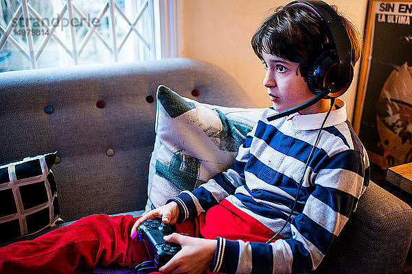 Junge sitzt auf dem Sofa  trägt ein Headset und benutzt den Game-Controller