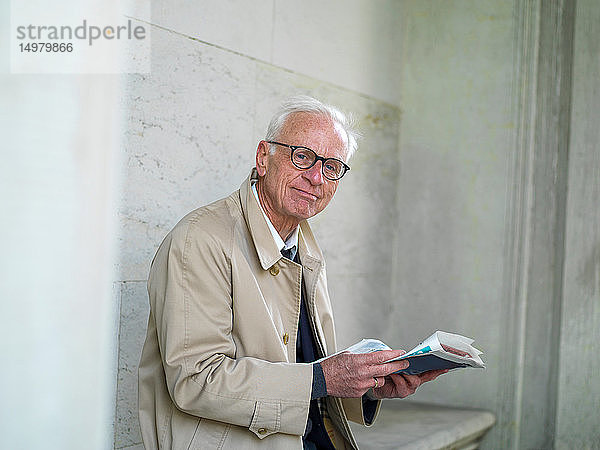 Älterer Mann im Regenmantel beim Zeitungslesen  Porträt  Kopenhagen  Hovedstaden  Dänemark